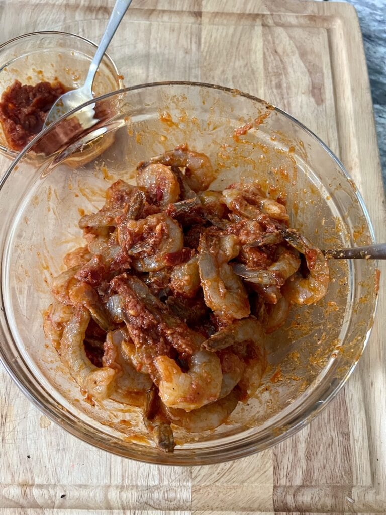 Stirring raw shrimp with spicy tomato marinade for shrimp fra diavolo recipe.