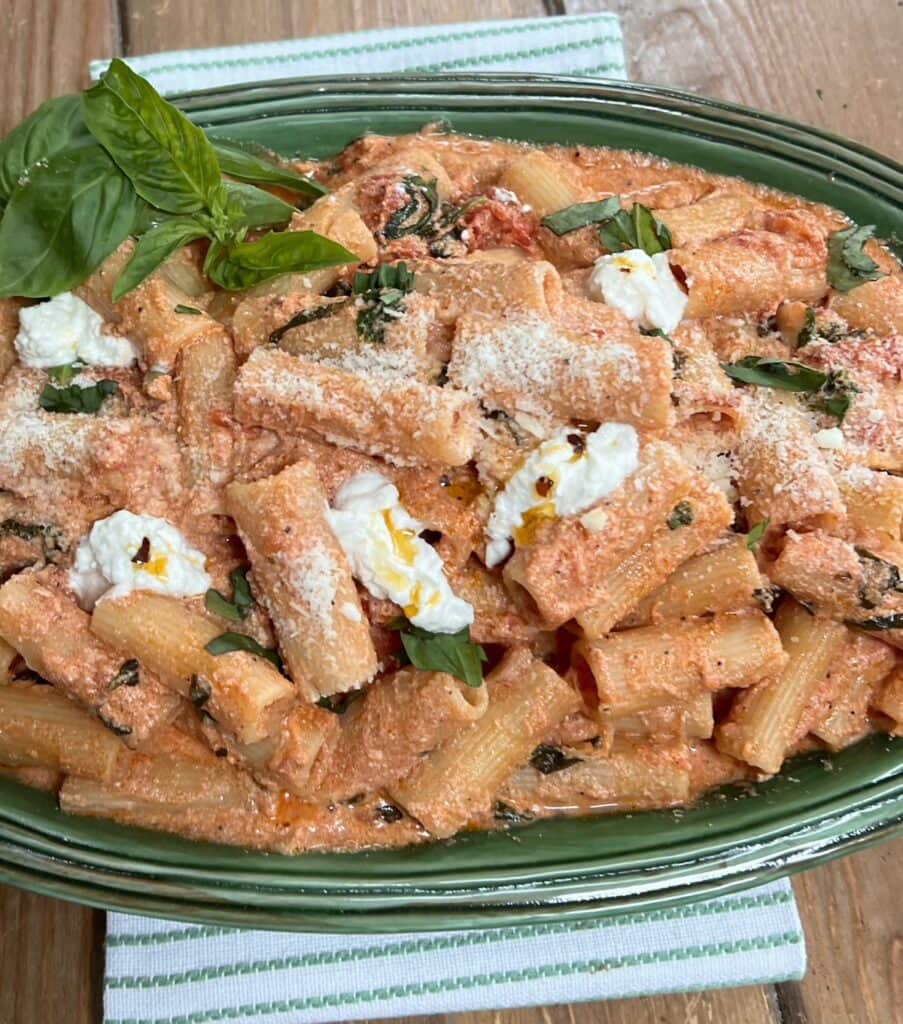 Creamy tomato ricotta pasta on green serving platter over decorative towel with fresh basil sprig garnish.