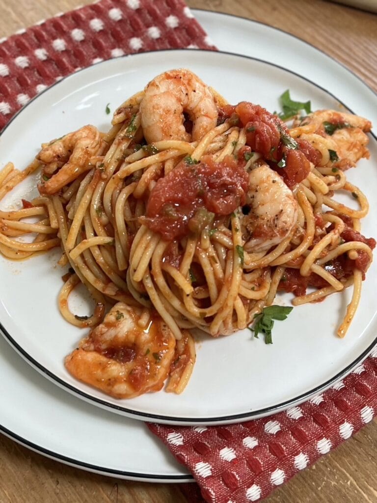 Spicy shrimp arrabbiata pasta on white dinner plate over red decorative towel.