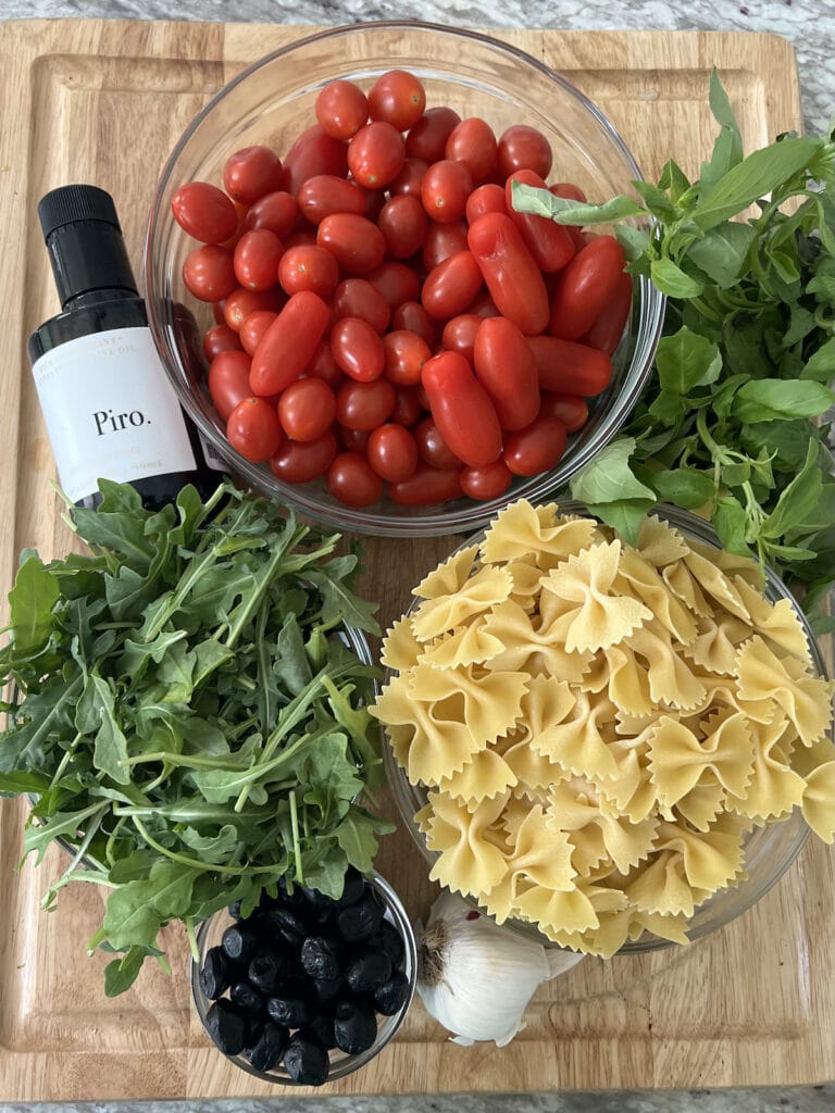 All ingredients for tomato pasta salad on cutting board.