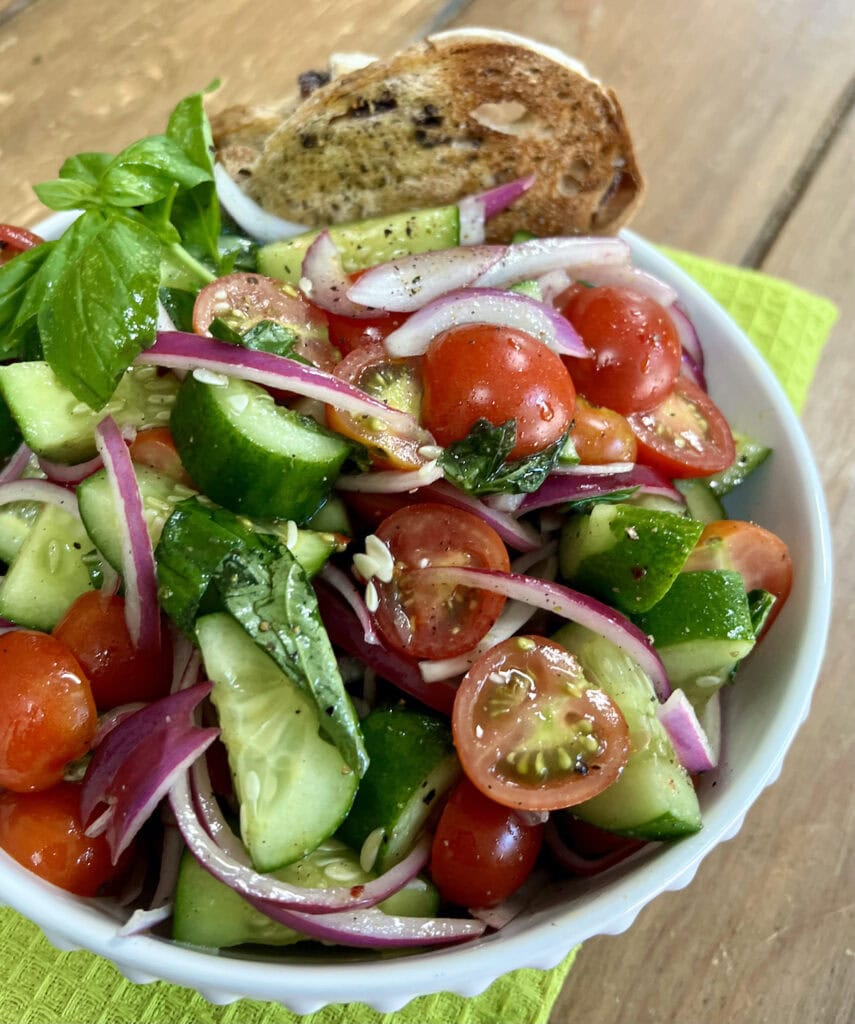 Italian Cucumber Tomato Salad in white bowl with some toasted bread over green towel.