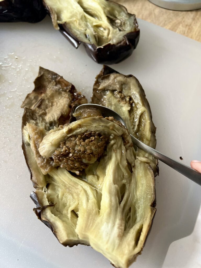 Scooping baked eggplant flesh out with a spoon.