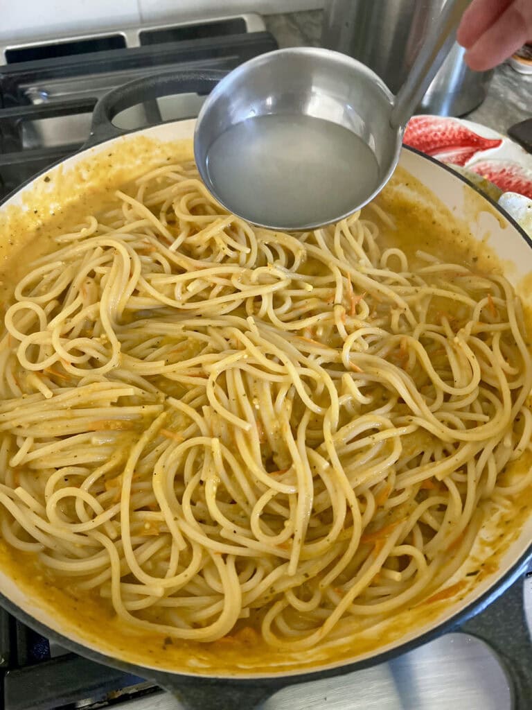 Adding some briny pasta water to spaghetti with yellow tomato sauce.