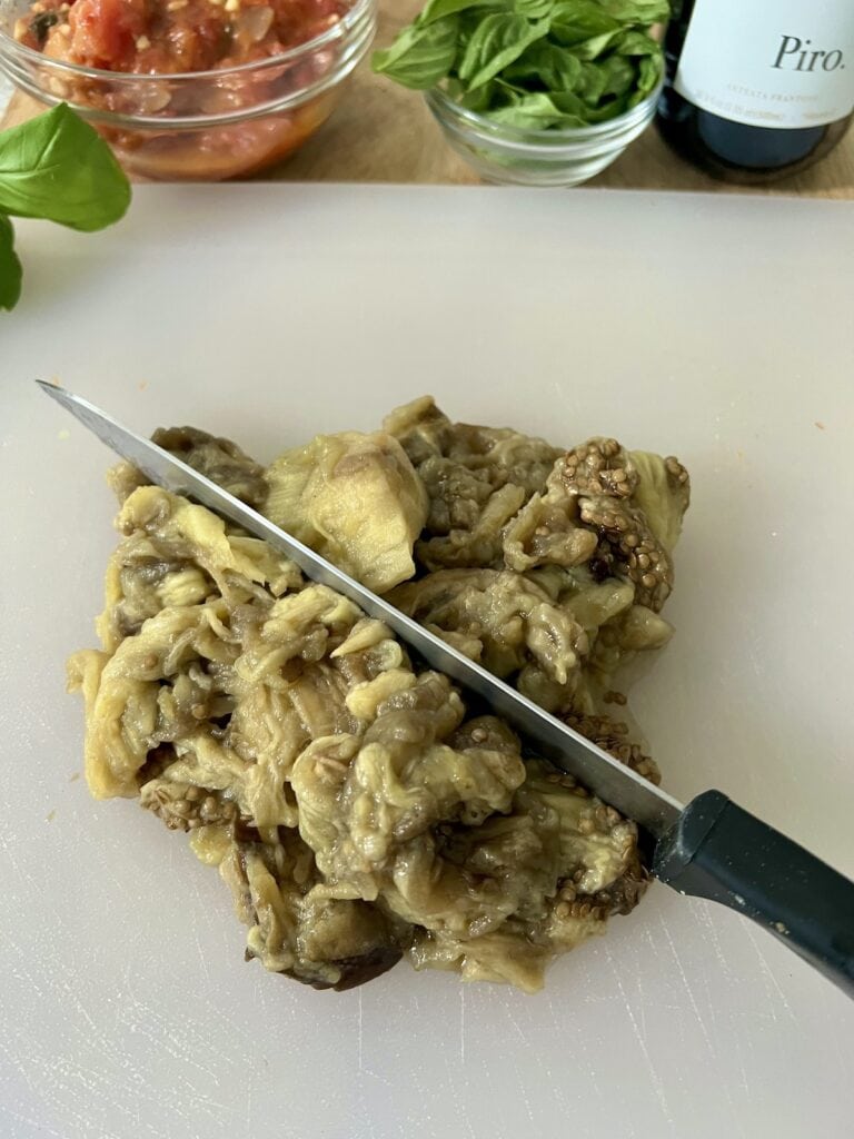 Chopping eggplant flesh on cutting board with knife.