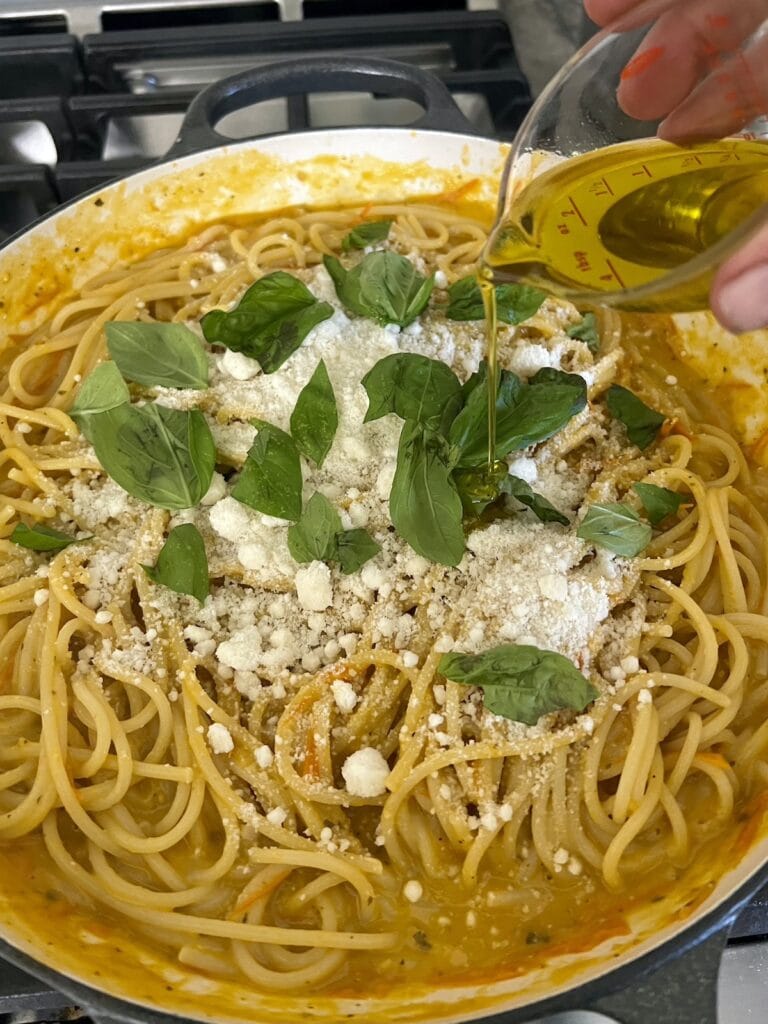 Pouring olive oil into pasta with sun gold tomatoes to finish it.