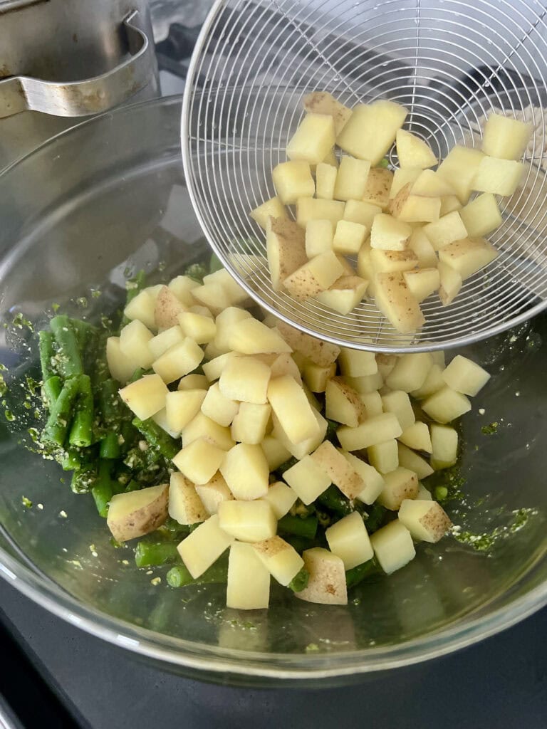 Adding cooked potatoes to bowl woth pesto and green beans.
