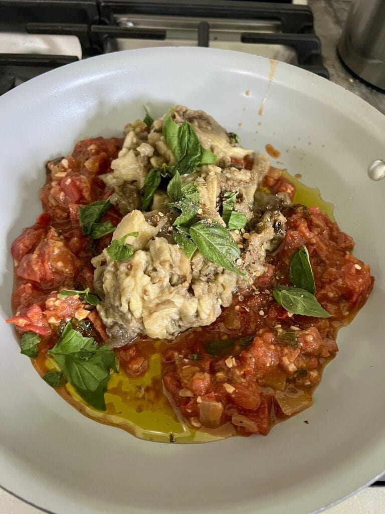 Roasted veggie mixture with olive oil and basil in pan to finish the roasted eggplant spread.