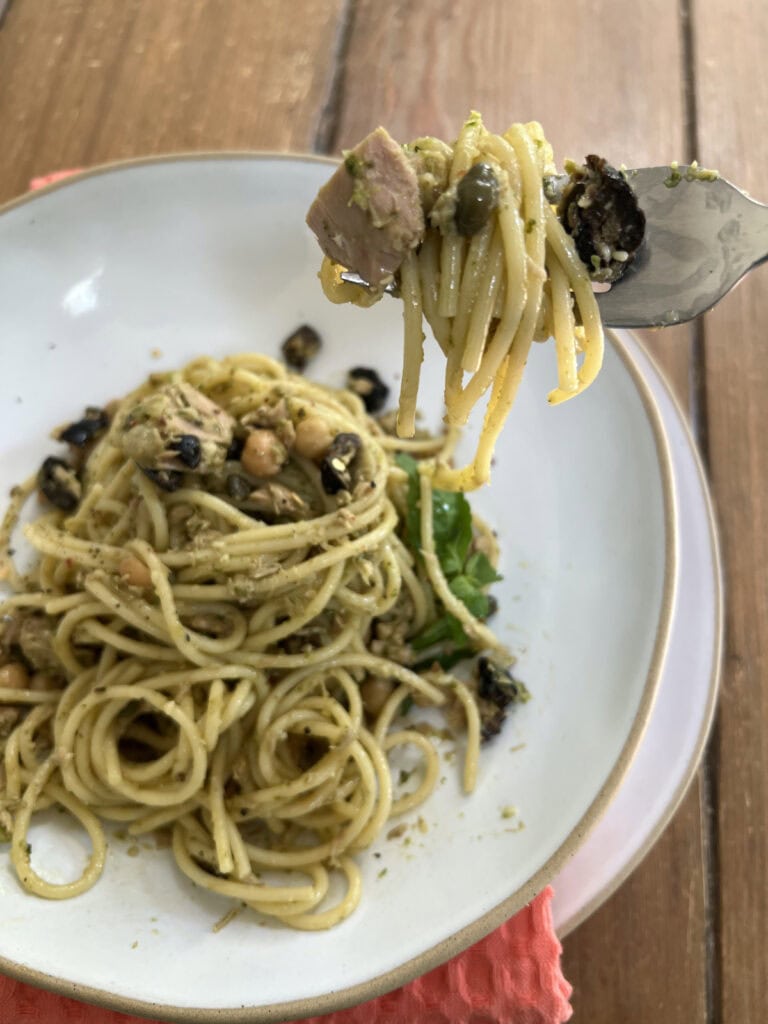 Forkful of tuna pasta with pesto being held above a bowl of it.