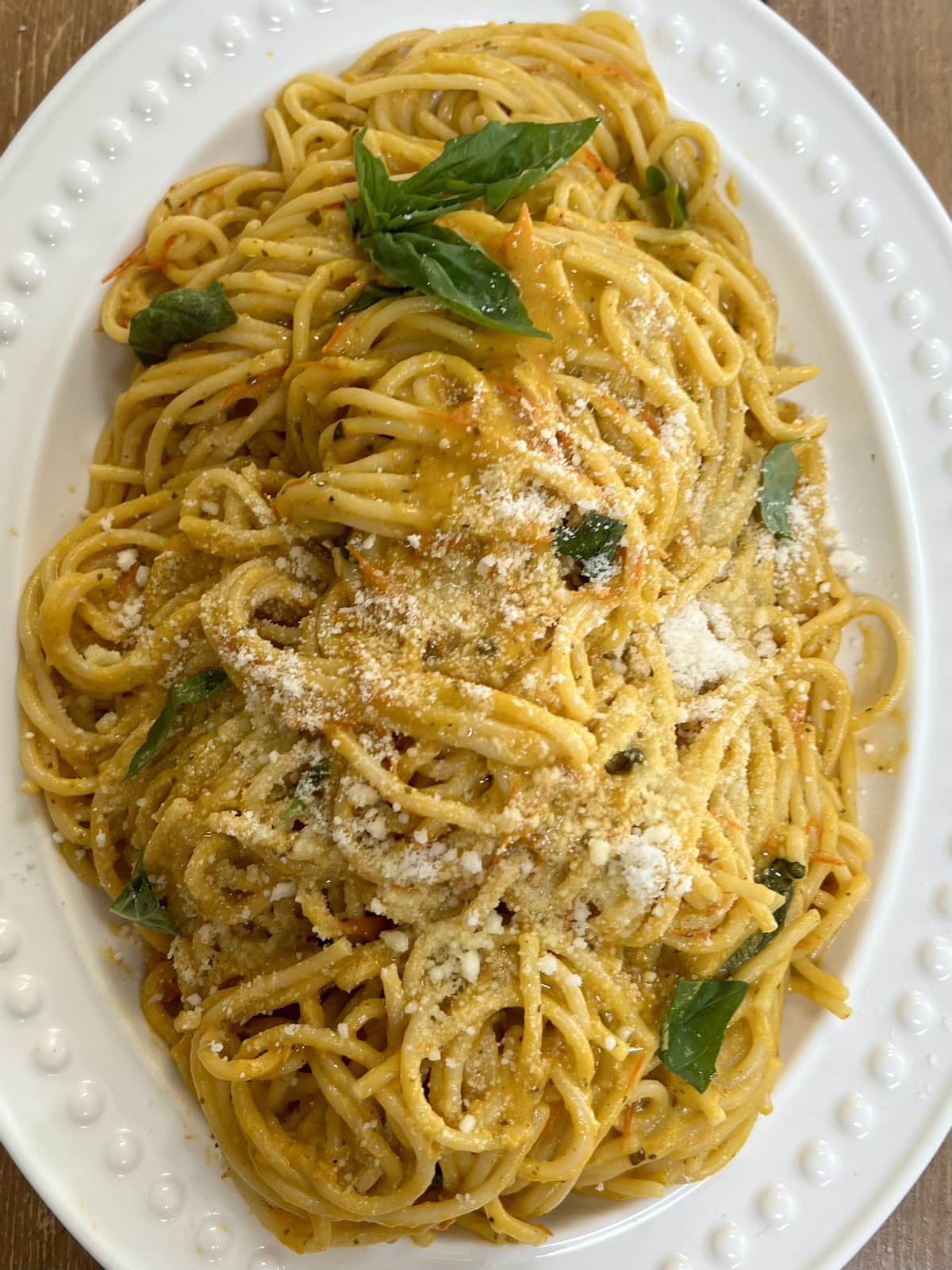 Spaghetti with yellow tomato sauce topped with some grated cheese in white serving platter over yellow towel.