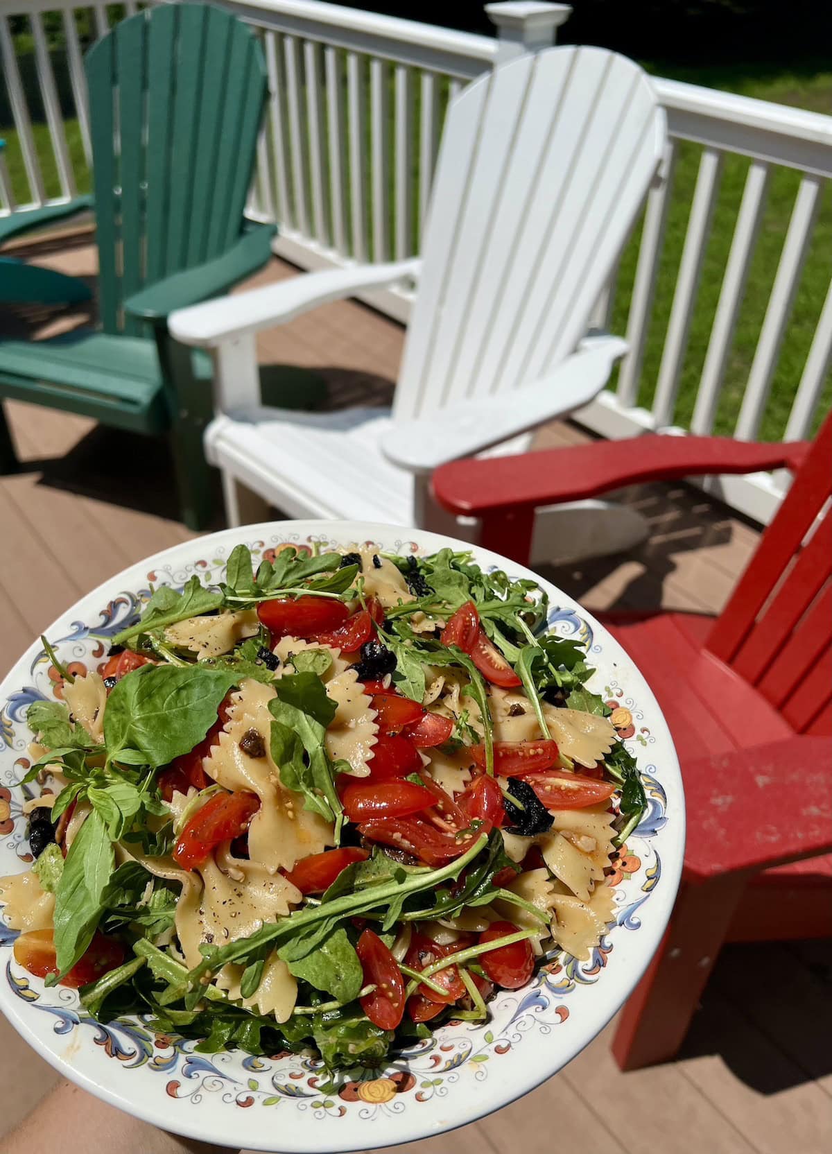 Bowl of tomato olive pasta salad with deck chairs in background.