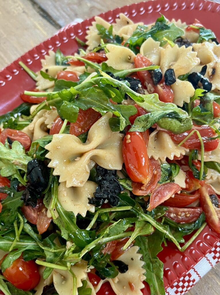 Close up of Italian tomato basil olive pasta salad in red serving platter.