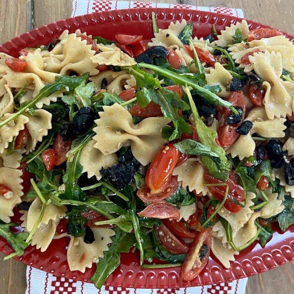 Tomato Basil Pasta Salad in red serving platter over decorative towel.