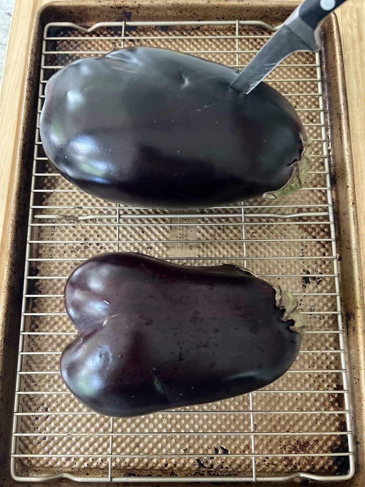 Piercing large eggplant with knife to make slits for roasting; eggplant on wire rack over cutting board.