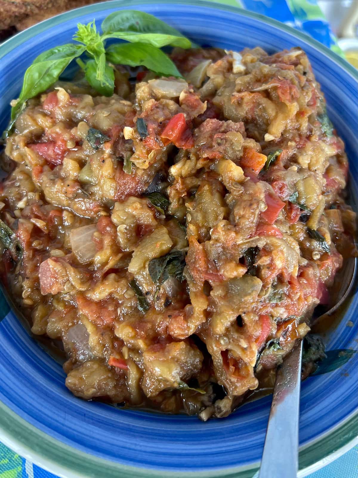 Roasted eggplant tomato spread with basil sprig garnish in blue serving dish.