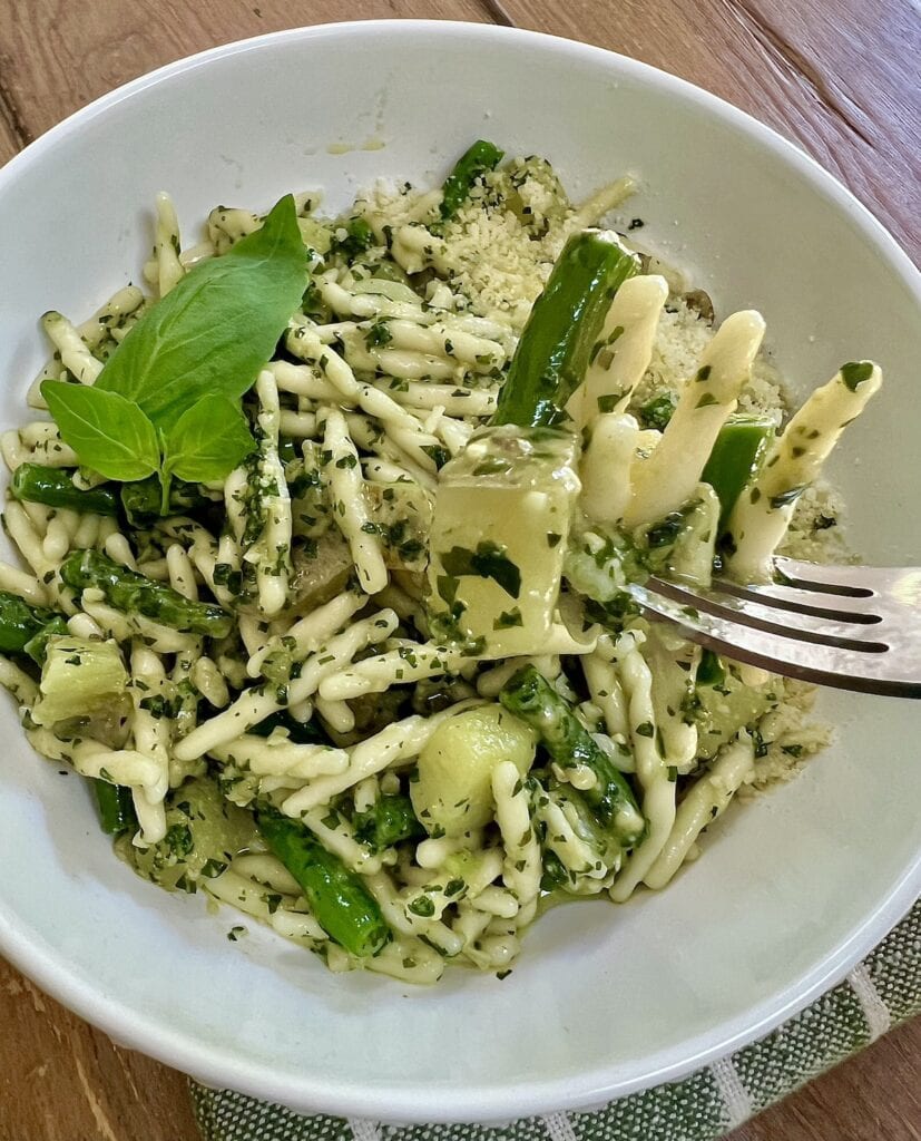 Close up of trofie al pesto genovese on fork over bowl of it.