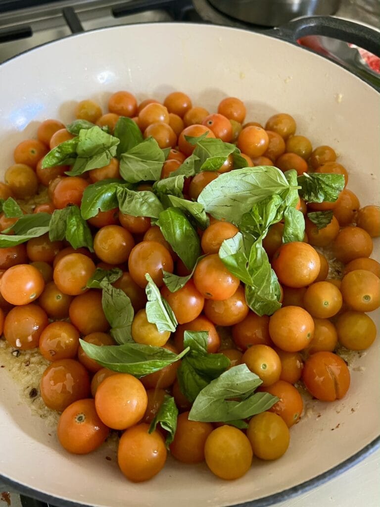 Fresh basil and sun gold tomatoes added to skillet with garlic, butter and oil.