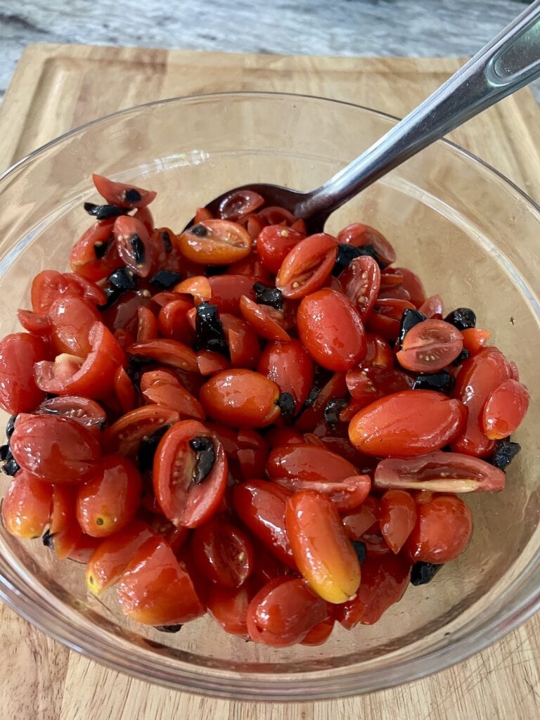 Tomato olive mixture in bowl with spoon for Italian bowtie pasta salad.