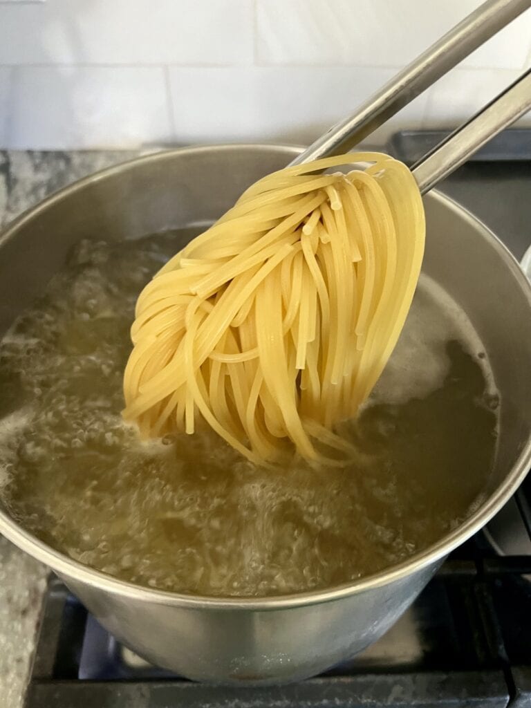 Cooking spaghetti being held up by tongs over boiling water in pot.