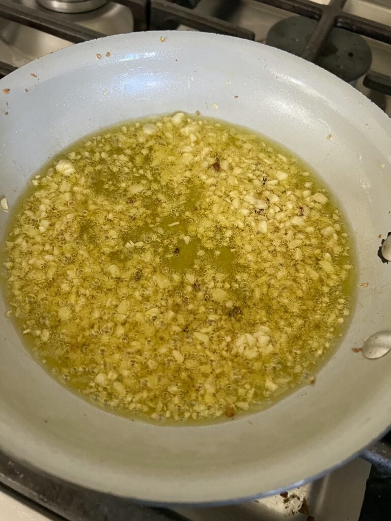 Cooking chopped garlic in small pan for tomato basil pasta salad.