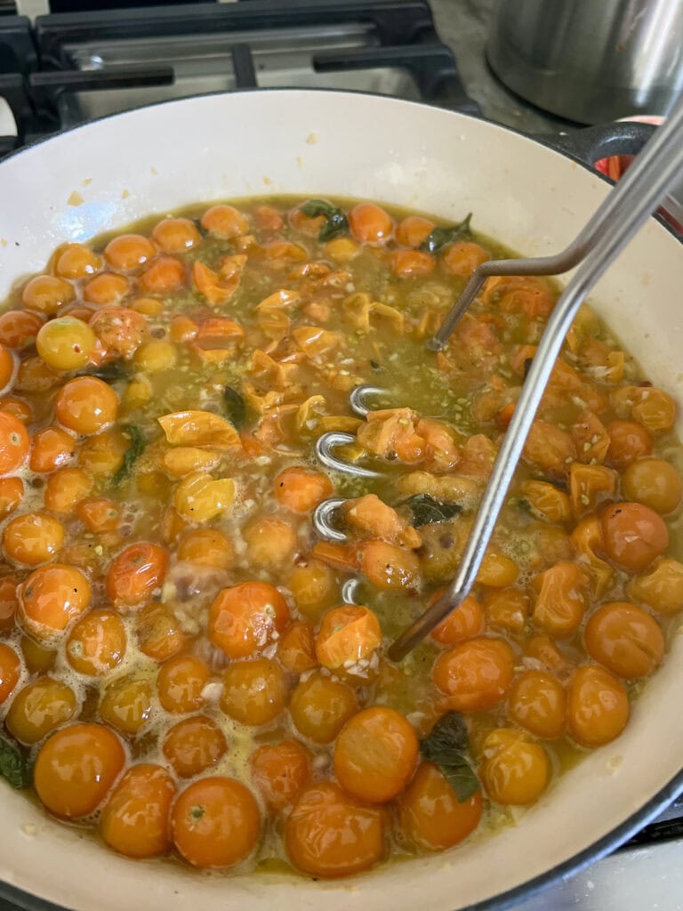 Smashing the burst yellow cherry tomatoes (sun gold toamtoes) in skillet with a potato masher.