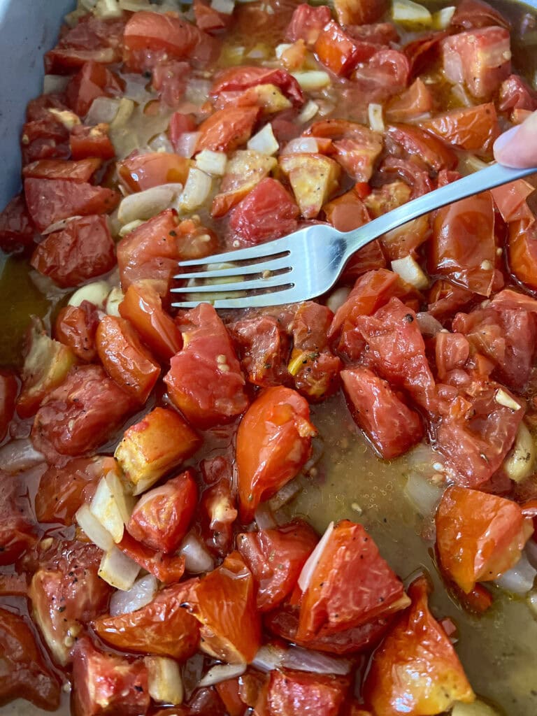 Roasted tomato mixture being smashed with a fork.