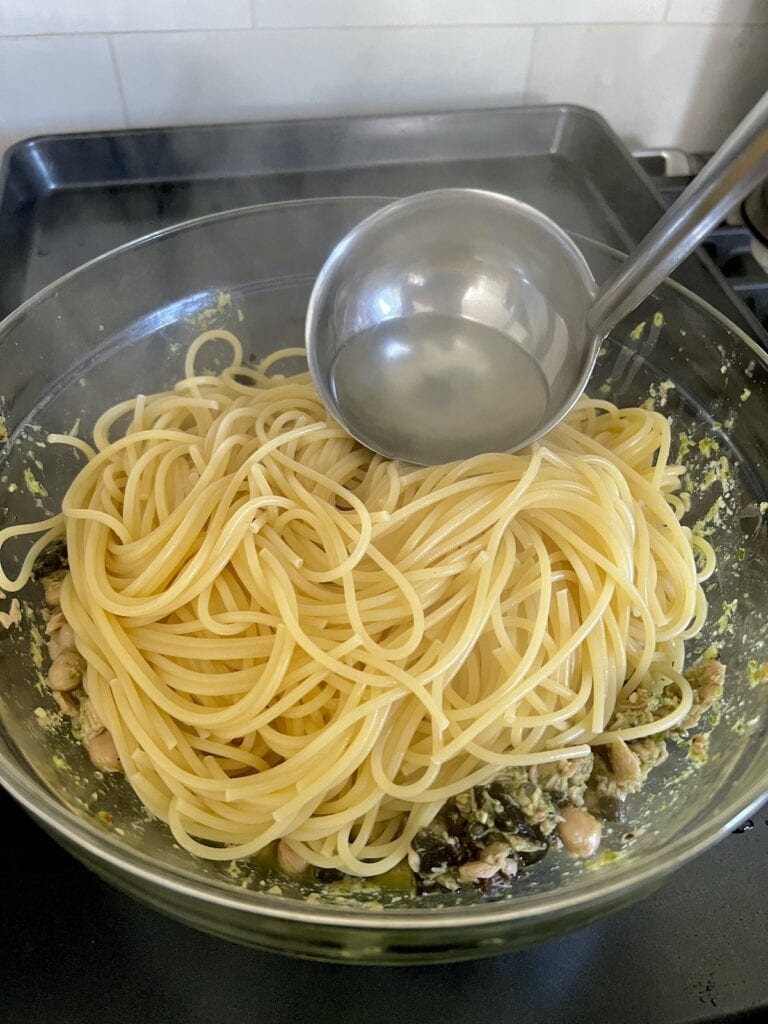 Finishing the tuna pesto pasta with a little pasta water bing ladled into it.