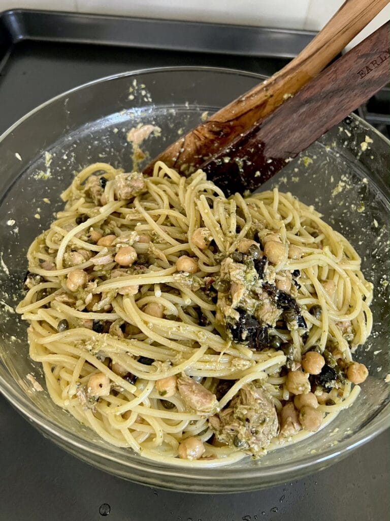 Mixing the tuna pasta with pesto with a wooden utensil in glass bowl.
