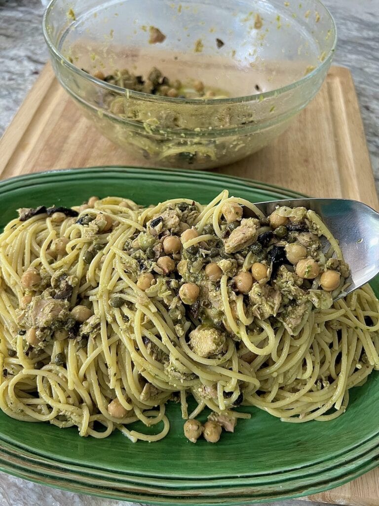 Plating the tuna pesto pasta into green serving platter from bowl using a stainless steel spoon.
