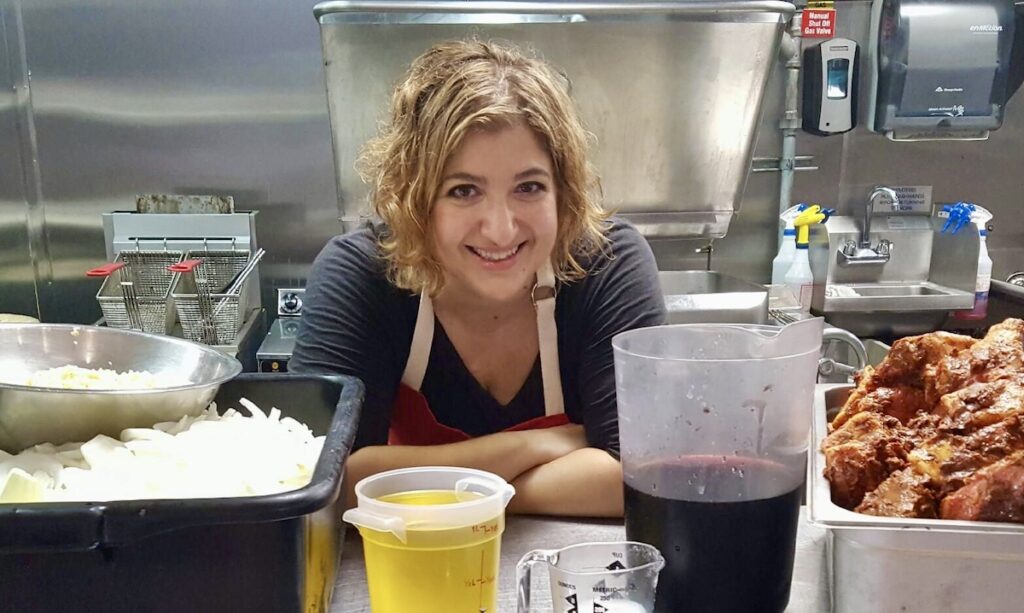 Michele at work in professional kitchen amongst large containers of food.