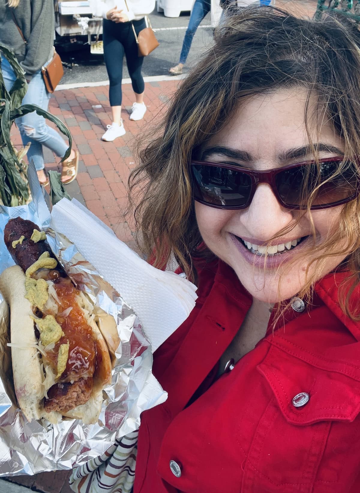 Michele in sunglasses holding a sausage sandwich.