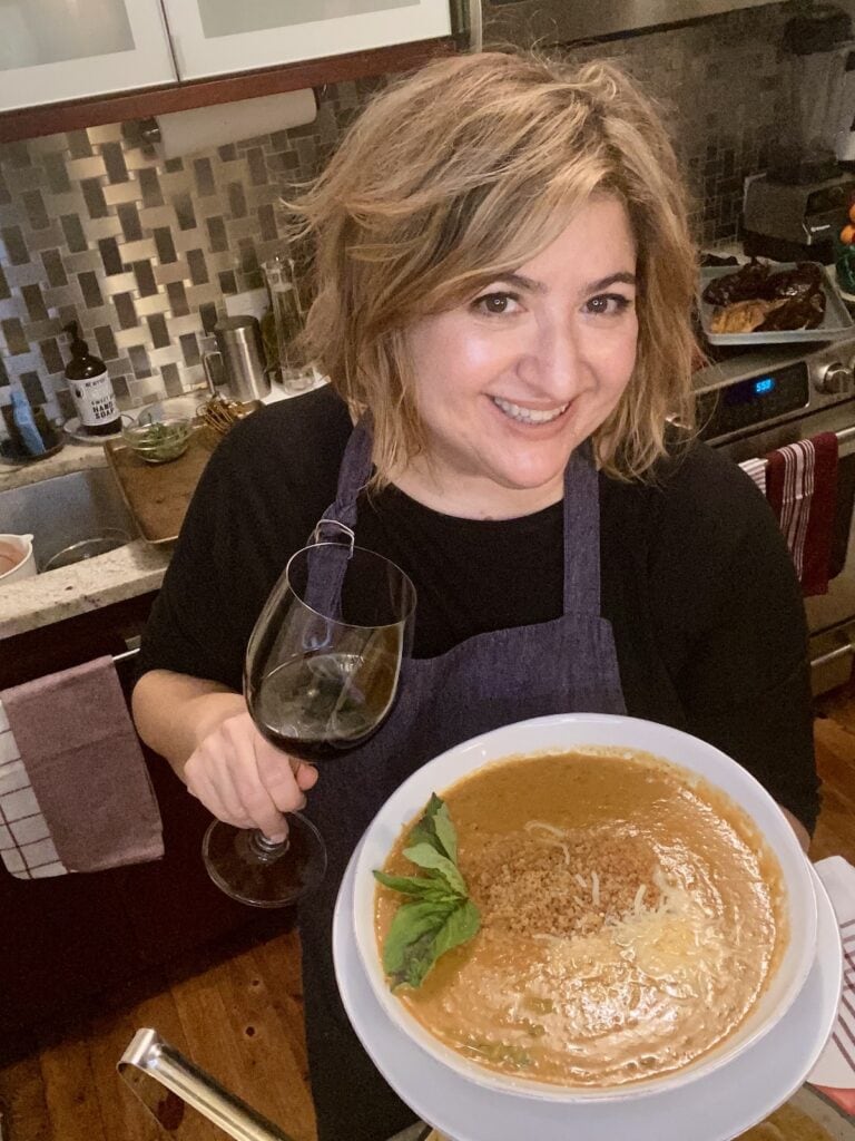 Michele holding glass of wine and bowl of soup.
