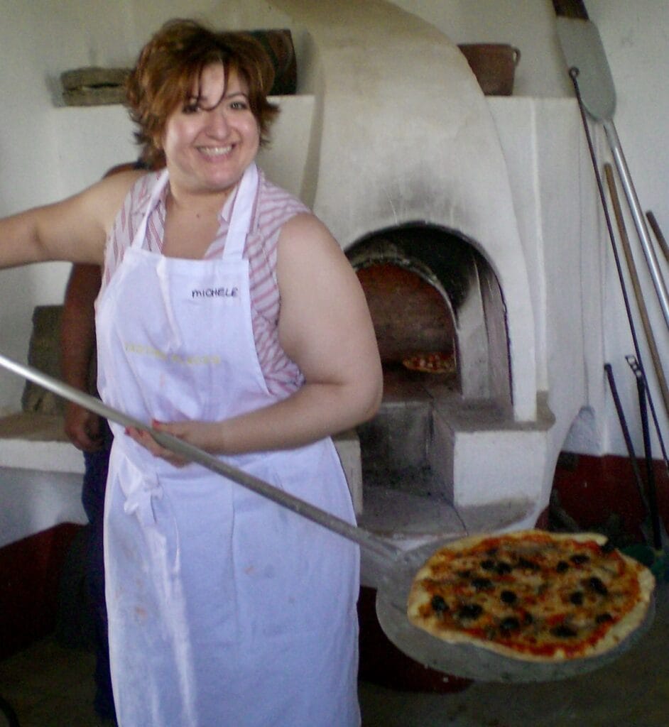 Michele holding a paddle with pizza in front of pizza oven in Italy.