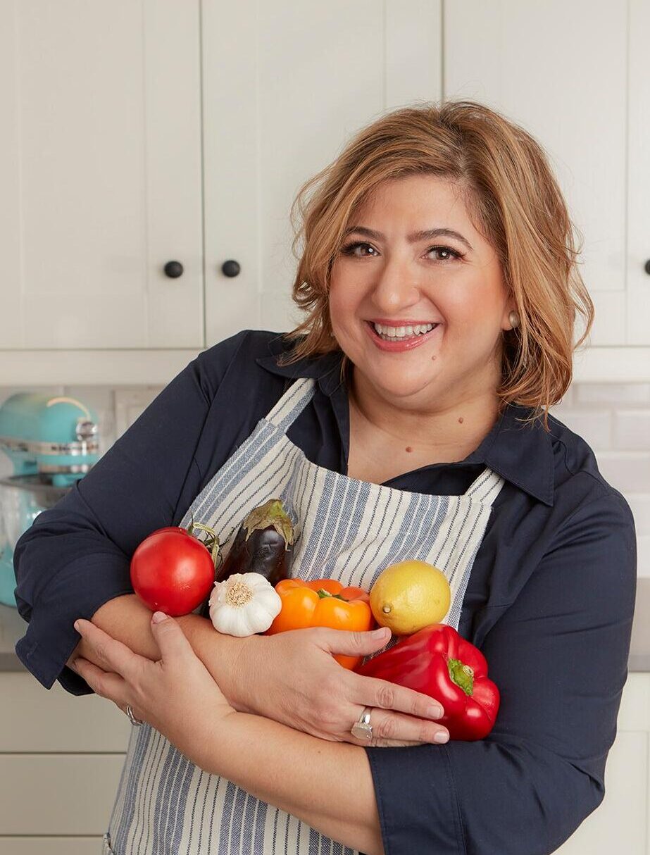 Michele in apron holding several vegetables.