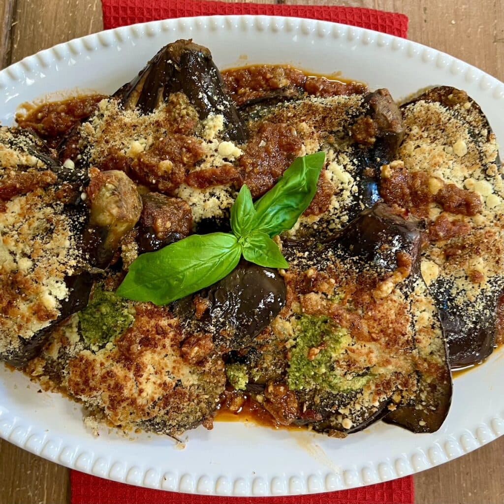 Hasselback Italian eggplant on white serving platter with basil sprig.