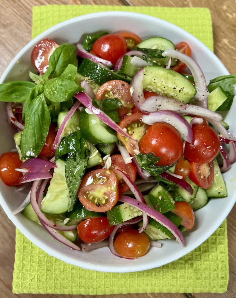 Italian Cucumber Tomato Salad in white bowl on green towel.