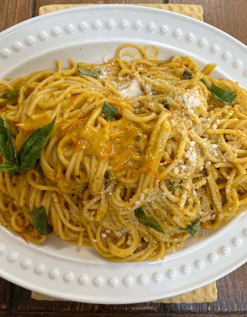 Pasta with Sun Gold Tomatoes topped with some grated cheese in white serving platter over yellow towel.