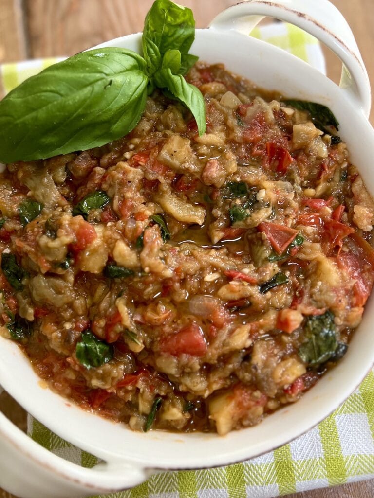 Roasted eggplant spread with basil sprig garnish in white serving dish.