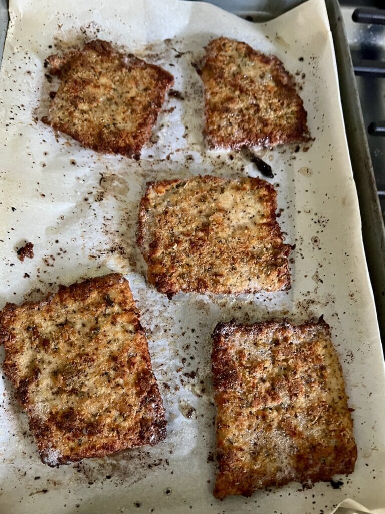 Five pieces of baked pork cutlets on parchment paper-lined sheet pan.