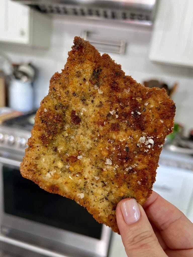 Close up of crispy Italian pork cutlet being held in hand in front of stove.