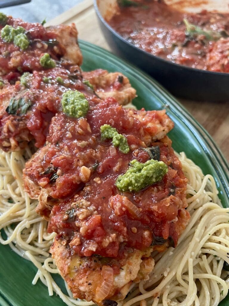 One Pan Chicken Pomodoro over a bed of spaghetti with garlic and olive oil, topped with a few spoonfuls of basil pesto.