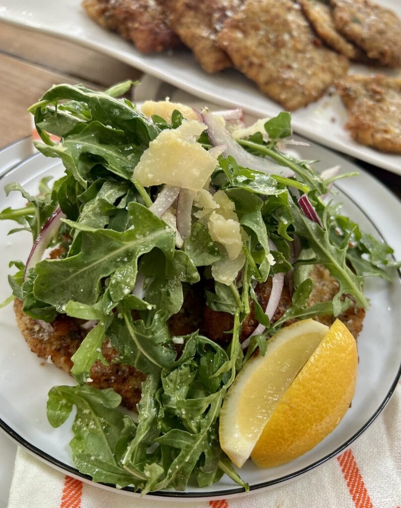 Crispy pork milanese served the classic way–topped with a simple arugula salad with red onion and shaved Parmigiano-Reggiano cheese, served with lemon wedges.