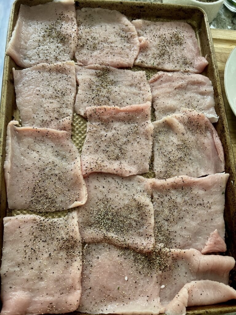 Pieces of pork that have been patted dry and seasoned with salt and black pepper on a sheet pan.
