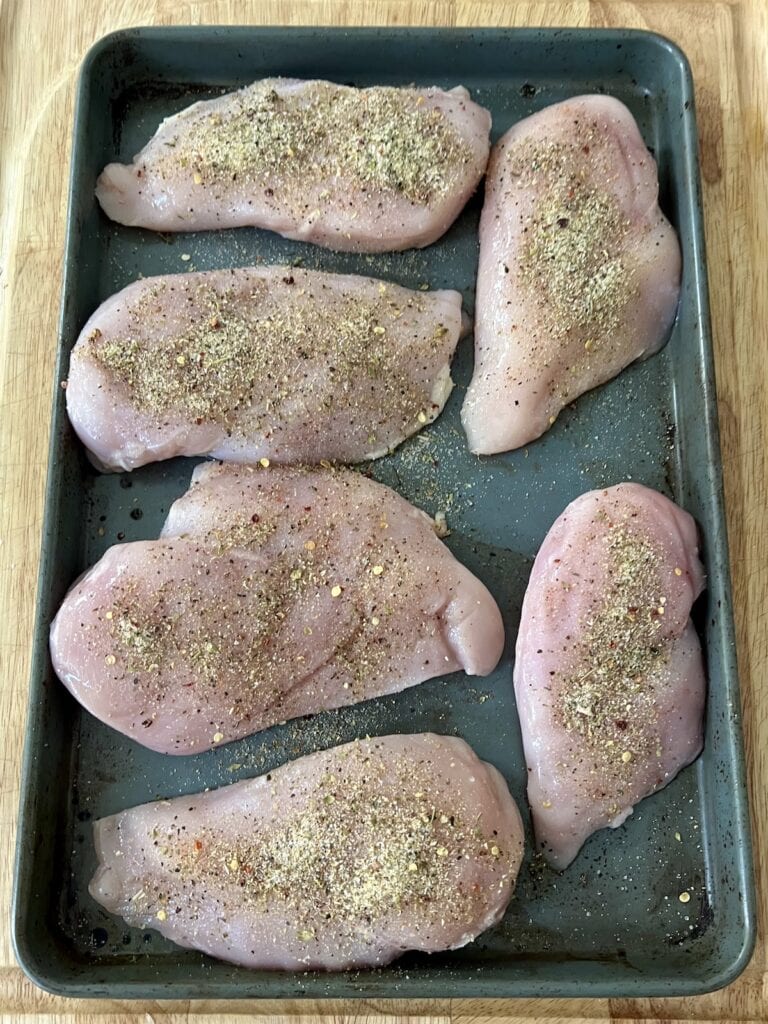 Chicken breasts sprinkled with salt and pepper on baking sheet.