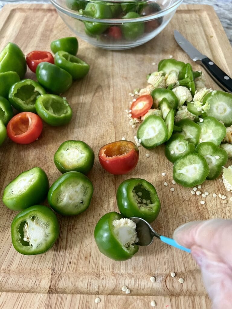 Using a spoon to scoop out the seeds and membrane from inside pepper.