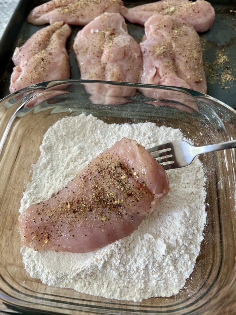 Coating one chicken breast in flour using fork.