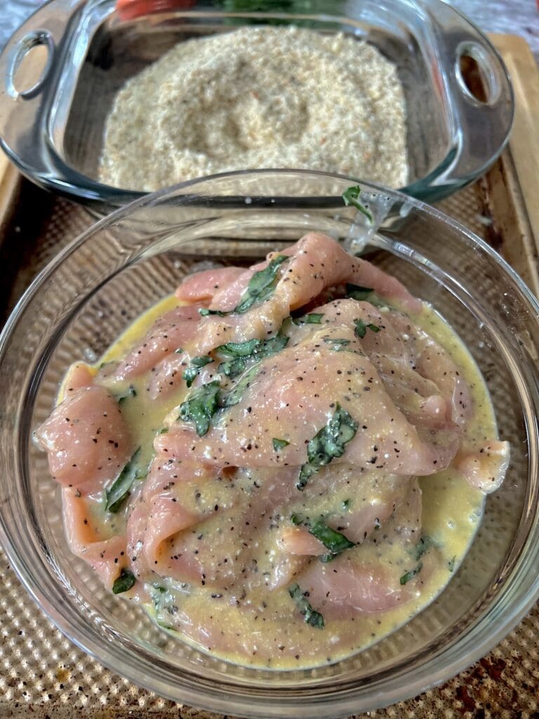 Bowl of thin pork in seasoned egg and milk mixture next to a pan of seasoned breadcrumbs.