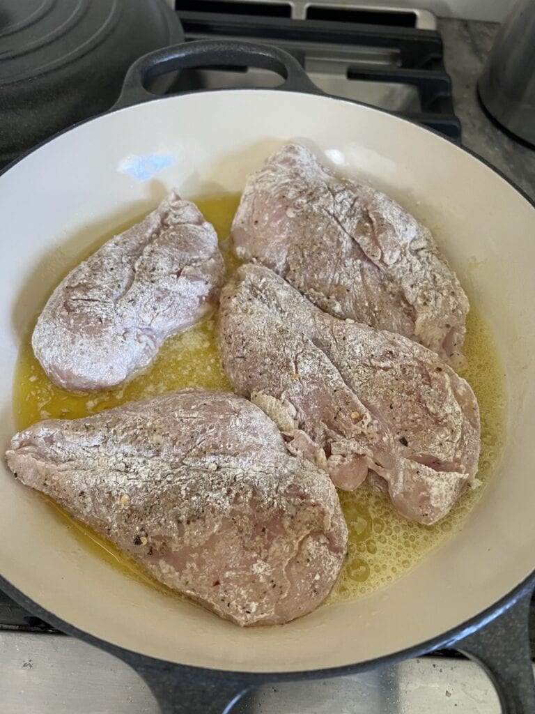 Searing the seasoned and floured boneless, skinless chicken breast in an oil and butter combination in pan.