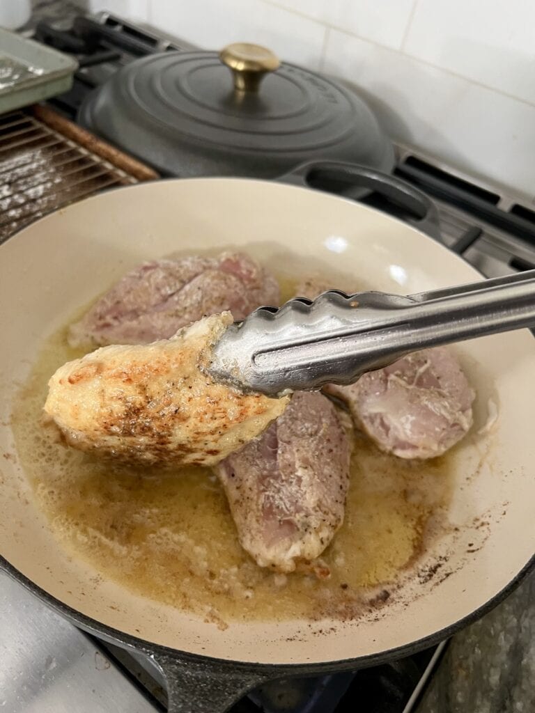 Turning one chicken breast over in pan after browning first side.