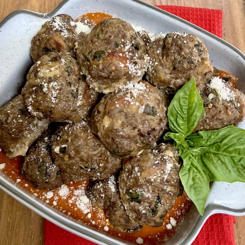Eggplant and beef meatballs in serving dish with basil garnish.