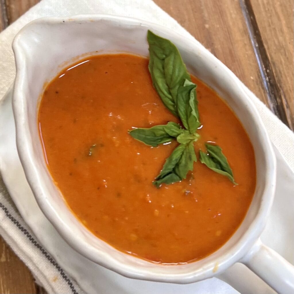 Homemade cherry tomato sauce in white gravy dish with basil garnish.